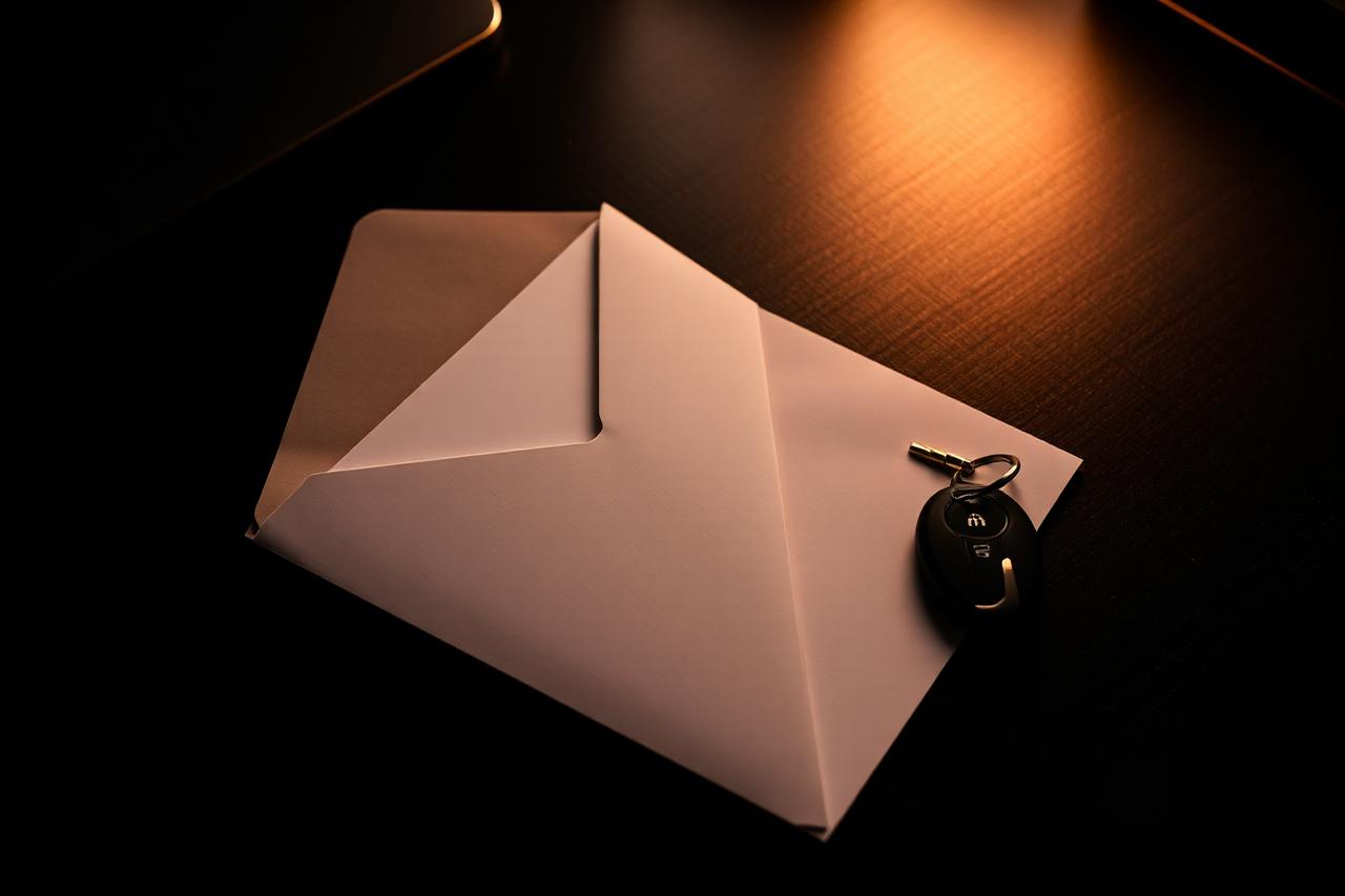 Opened envelope and folded notice letter on a dark desk beside car keys