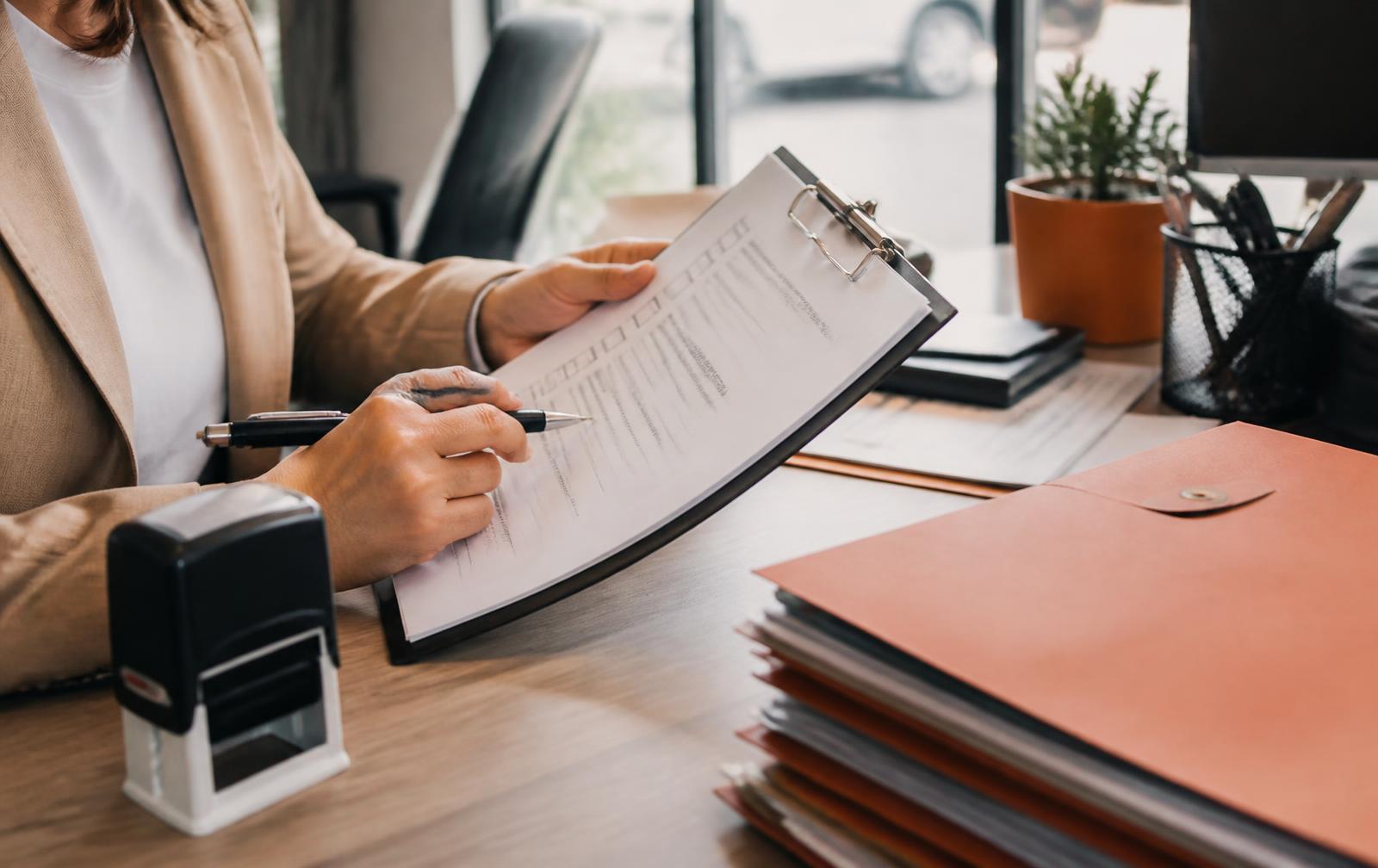 Title clerk reviewing a checkbox disclosure form on a clipboard beside stacked vehicle title folders